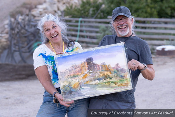 Lisa Bryant and Ward Stroud make excited poses as they hold their canvas landscape painting outside in Escalante.