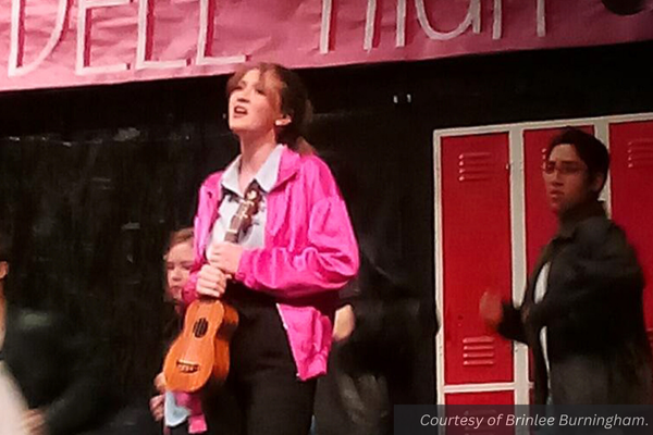 A girl in a pink jacket sings holding a ukulele. Courtesy of Brinlee.