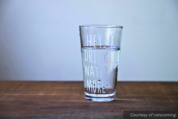 A glass full of water with the words "hey, drink more water" printed on the outside. Courtesy of catscoming.