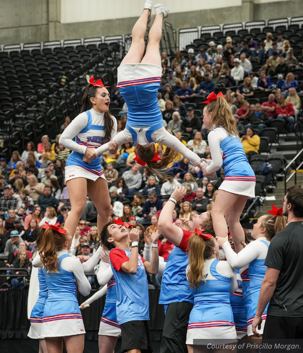 A Piute cheerleader flies through the air held by the arms by two other stunt groups. Courtesy of Priscilla Morgan.