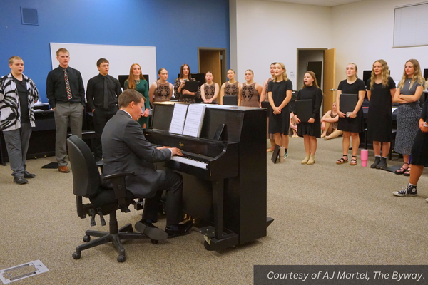 Piute's choir stands in a bow shape singing together as Tyrel Ivie plays the piano. Courtesy of AJ Martel, The Byway.