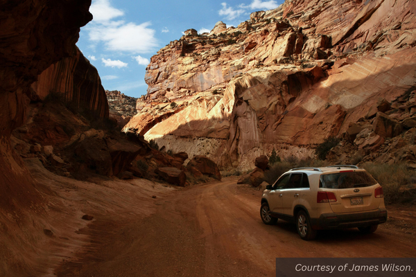 A car going through a shaded canyon on a red dirt road. Courtesy of James Wilson.