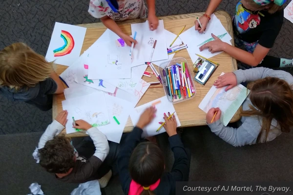 A few kids sit at a low table and color pictures. Courtesy of AJ Martel, The Byway.